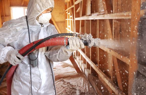 Worker sprays insulation in building frame.