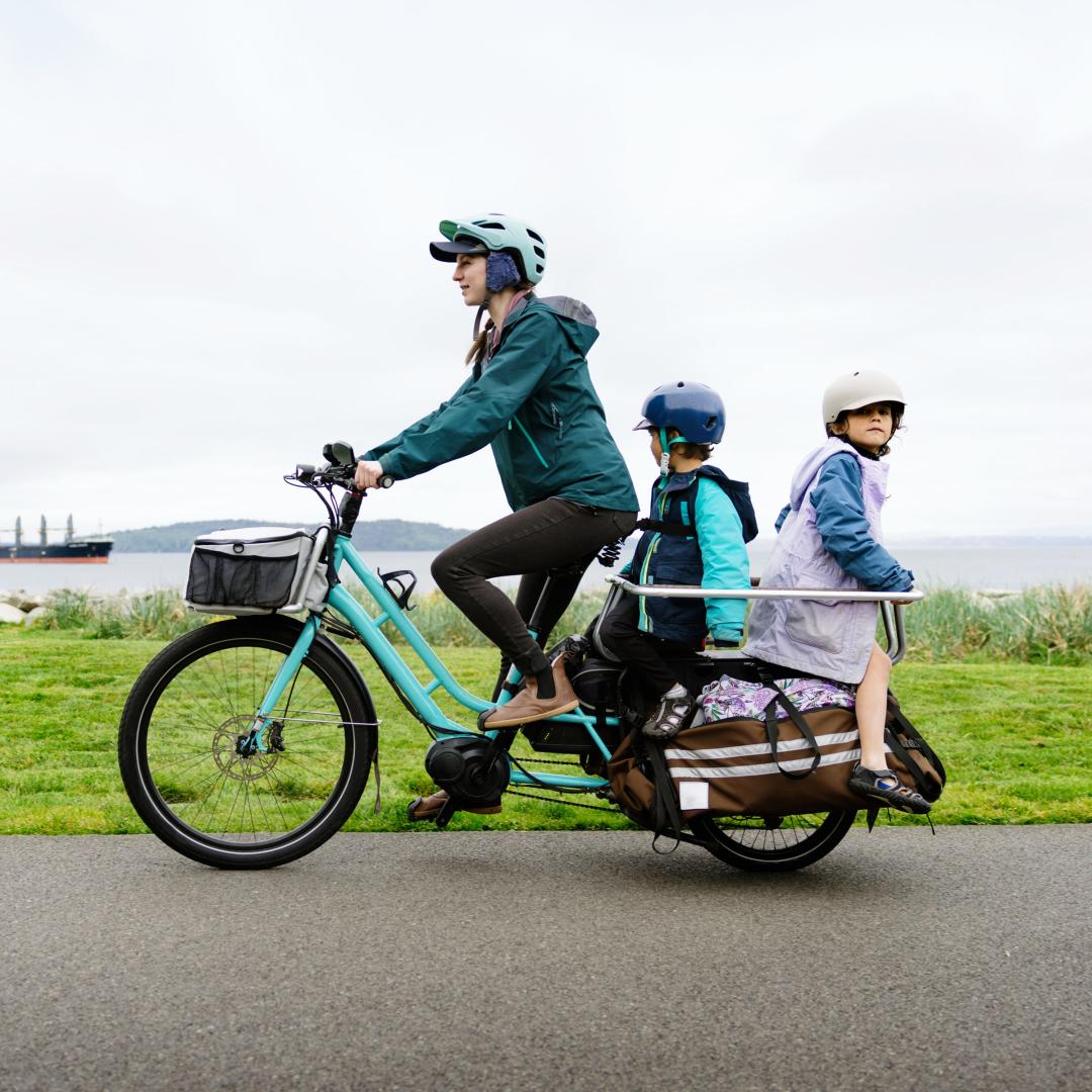Parent riding electric bicycle with children seated in back carrier